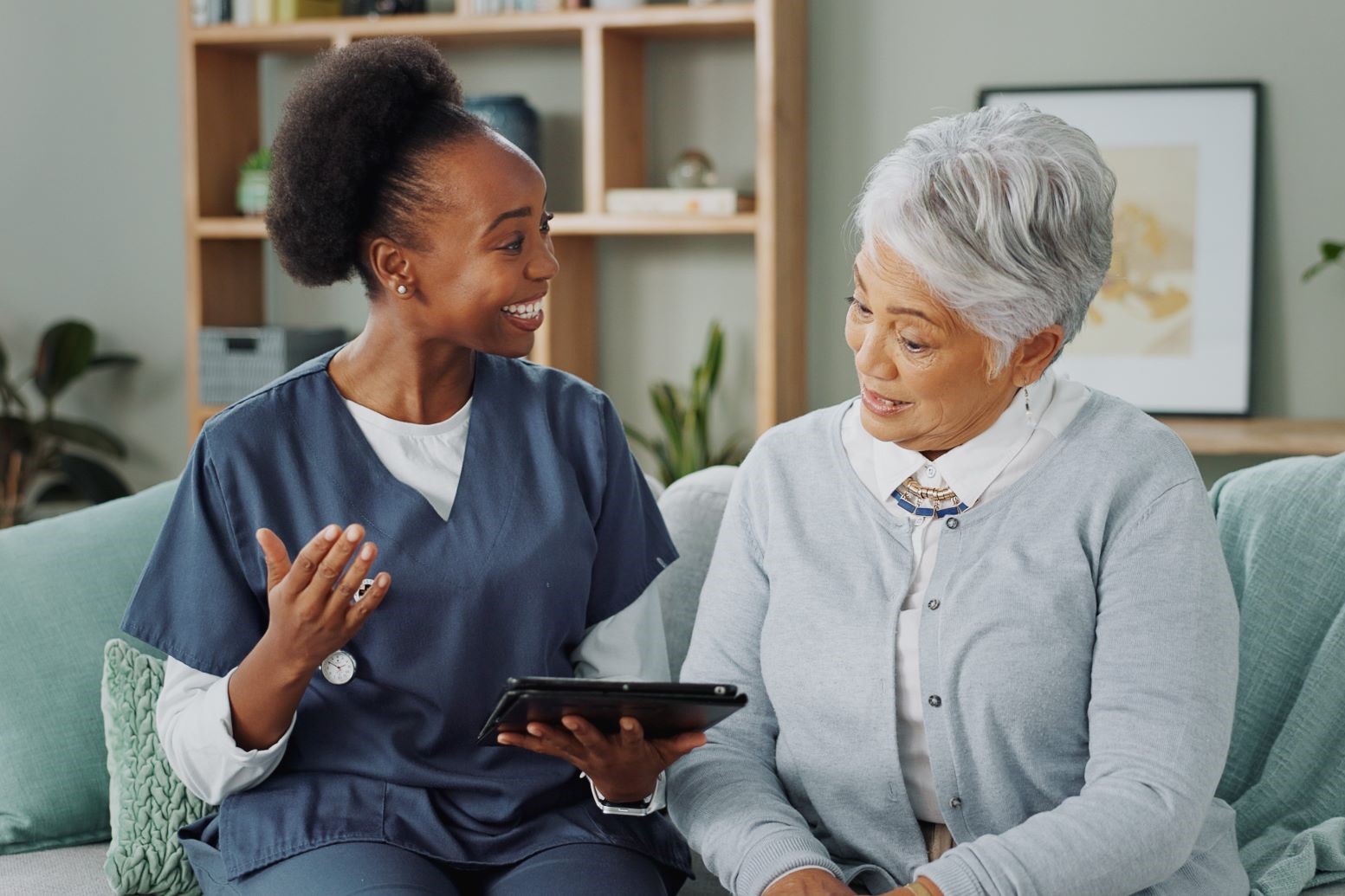 happy-nurse-senior-consulting-with-tablet-sofa-healthcare-communication-consultation-home-medical-caregiver-helping-talking-elderly-female-person-with-technology-advice-2